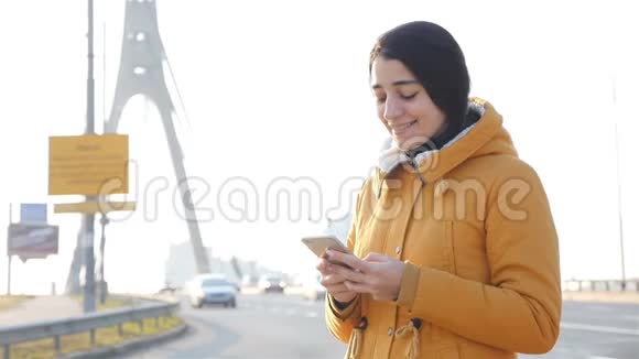 一个女孩站在桥的背景上在智能手机上写入消息慢动作视频的预览图