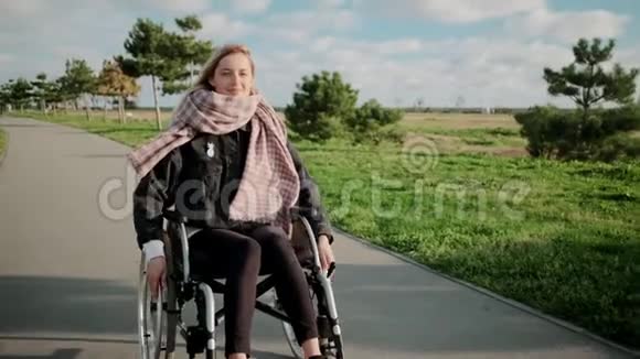 患有腿部和脊柱疾病的女人正坐轮椅在公园里微笑着视频的预览图