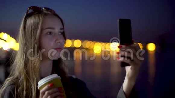 自拍的女孩深色头发戴着一杯纸杯咖啡嚼着口香糖微笑着在镜头前眨眼视频的预览图