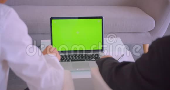 两位商人在办公室使用带有绿色屏幕的笔记本电脑和握手协议的特写后景肖像视频的预览图