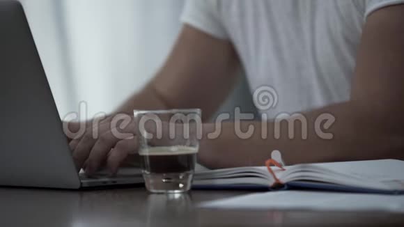 穿着白色t恤手提电脑和文件在家或办公室喝咖啡的无名男子他就是视频的预览图