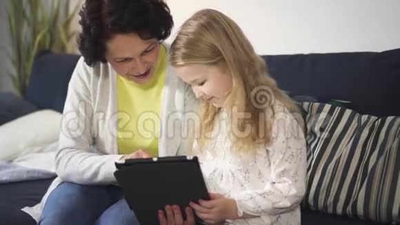 女人和女孩坐在沙发上使用新的数字技术平板电脑视频的预览图