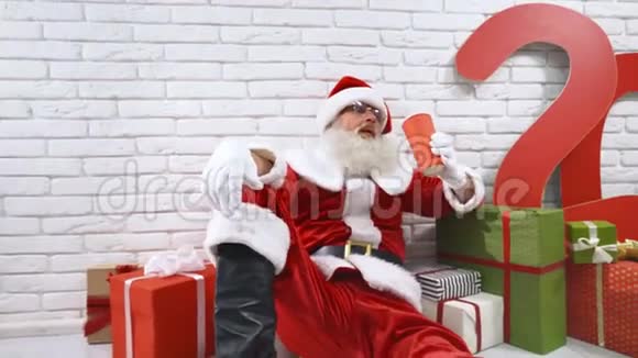 成熟的圣诞老人在地板上喝红杯子里的苏打水视频的预览图