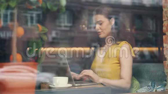 咖啡馆里使用笔记本电脑的女学生微笑着触摸键盘视频的预览图