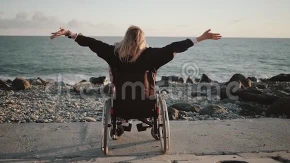独自一人的残疾妇女坐在轮椅上手举在海上海岸视频的预览图