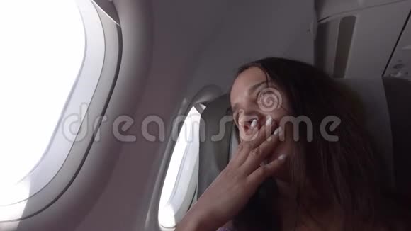 迷人的疲惫的年轻女子打哈欠关上窗户舷窗睡在飞机窗口附近视频的预览图