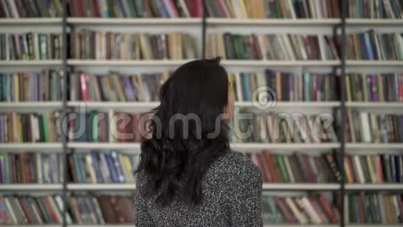 黑发女人的后视图指向书架上的一本书视频的预览图