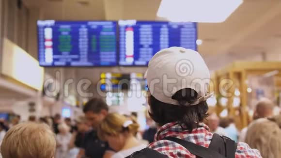 背包旅客在国际机场到达大厅内查看数字航班时刻表显示的航班信息视频的预览图