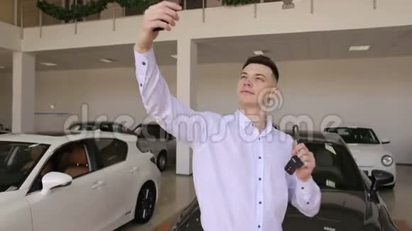 快乐男人在展厅里的新车前拿着钥匙自拍视频的预览图