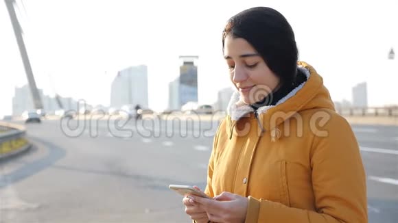 漂亮的女孩在智能手机上写信息慢动作背景公路视频的预览图