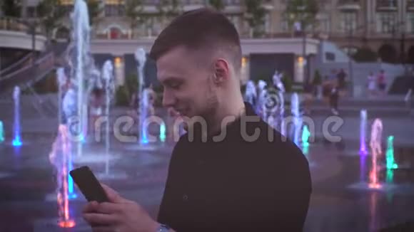 年轻迷人英俊年轻的欧洲白种人使用智能手机在霓虹灯喷泉灯光背景城市视频的预览图
