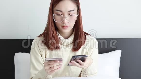 美丽迷人的聪明女人穿着黄色毛衣和眼镜用手机支付网上购物的信用卡视频的预览图