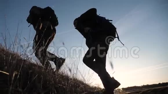 两名游客团队合作背包慢动作行走在夕阳的阳光下走着剪影两个视频的预览图