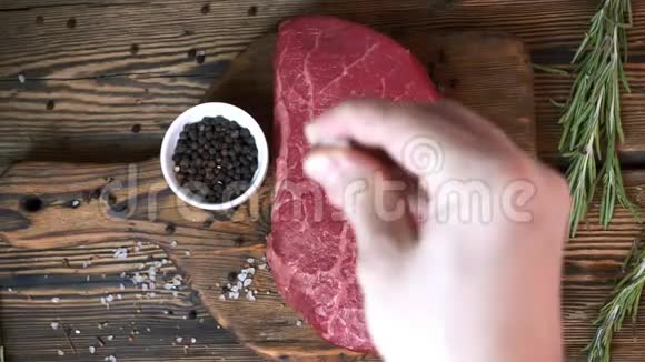 厨师盐生的新鲜牛排胡椒和迷迭香在木切割板上视频的预览图