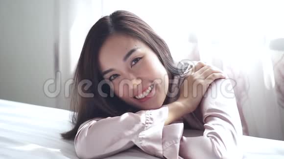 穿着性感粉色睡衣的幸福女人在卧室里看着镜头微笑视频的预览图