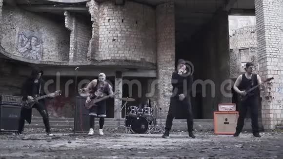 哥特式摇滚风格的摇滚歌手在废弃建筑的背景下用吉他和鼓包化妆演奏金属摇滚视频的预览图