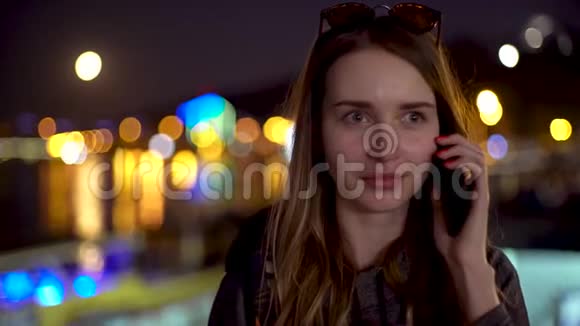 年轻女孩用她的智能手机看着相机带着闪闪发光的桥和大月亮在晚上微笑视频的预览图