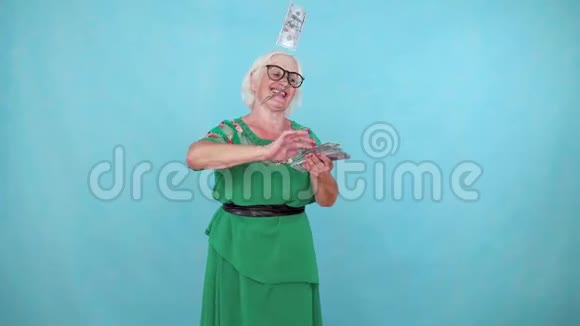 乐观向上的老妇人在蓝色背景上扔纸钞票视频的预览图