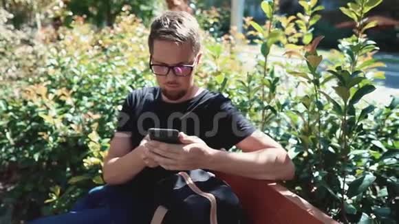 男人在公园的户外用智能手机浏览社交网络坐在长椅上视频的预览图