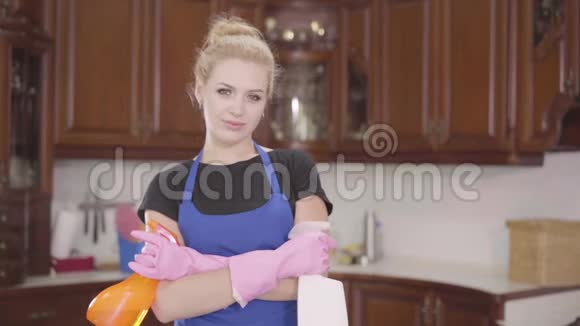 肖像可爱的年轻女子站在厨房里双手交叉地拿着洗洁精的瓶子看着镜头视频的预览图