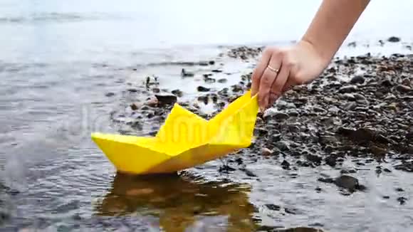 女人手把黄色的纸船放在水面上把它推开视频的预览图