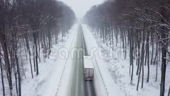 在大雪覆盖的冬季森林的道路上驾驶卡车的鸟瞰图视频的预览图