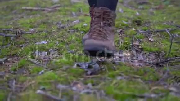 穿着靴子在森林里绿色苔藓上行走的女腿特写镜头视频的预览图