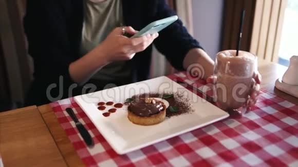 一个女孩用智能手机坐在时尚的咖啡馆里为她的热巧克力饮料拍照视频的预览图