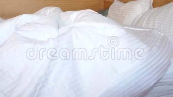 一个可爱的金发男孩躺在白色毯子下的床上头上盖着一条毯子视频的预览图