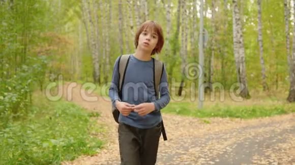 男孩少年背着背包走在秋天公园的绿树背景上帅气的少年男孩在路上视频的预览图