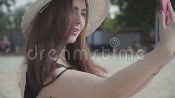 夏天戴着白色帽子的年轻女人在海滩上休息的手机上自拍的肖像夏日休闲视频的预览图