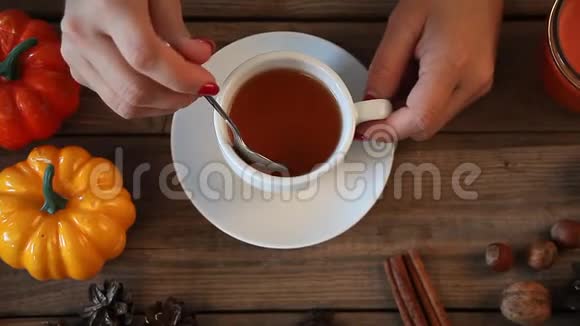 妇女手拿茶匙在木桌上搅拌热茶背景是南瓜树叶香料秋季大会视频的预览图