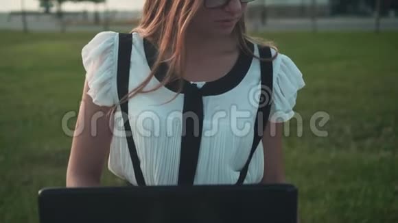商务女性穿着白色衬衫和眼镜坐在长凳上在笔记本电脑后面工作女孩在打电话视频的预览图