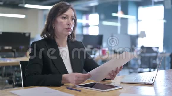 严肃的中年女商人在办公室里一边看报纸一边说话视频的预览图