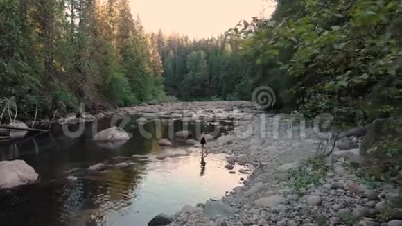 空中拍摄的一个迷人的年轻黑发女人在日落时分在一条原始的森林河流上跳过石头视频的预览图