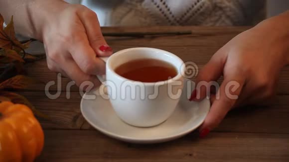女人手拿着把白色的茶杯放在老木桌上背景上有南瓜树叶香料秋天的概念视频的预览图