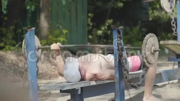 运动员举起杠铃躺在公园的长凳上锻炼肱二头肌保持身体的形状健身视频的预览图
