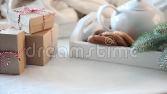 女人手把一杯咖啡或茶放在白色的桌子上上面有圣诞饼干茶壶礼品盒视频的预览图