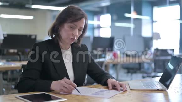 严肃的中年女商人在办公室工作时阅读文件视频的预览图