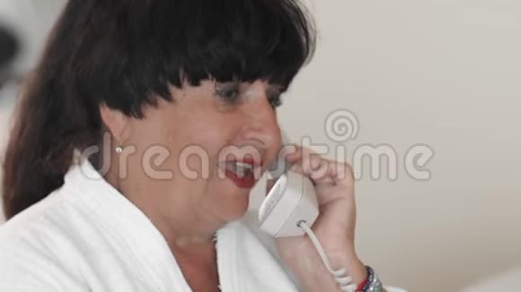 快乐的高级女人穿着白色浴袍在电话里讨论挂断了电话慢动作视频的预览图