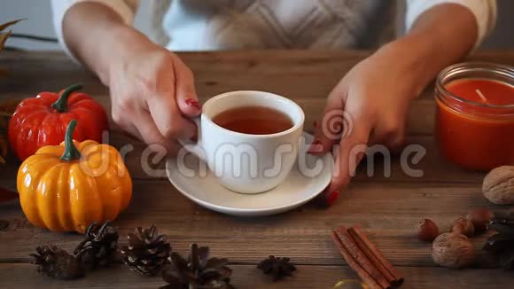女人手拿着把白色的茶杯放在老木桌上背景上有南瓜树叶香料秋天的概念视频的预览图