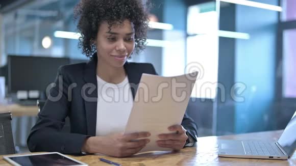 成功的非洲女商人在办公室阅读文件并用手势庆祝视频的预览图