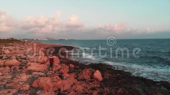 漂亮的女摄影师在美丽的粉红色日落中与霍里的帕福斯市拍摄巨大的海浪和岩石海岸的照片视频的预览图