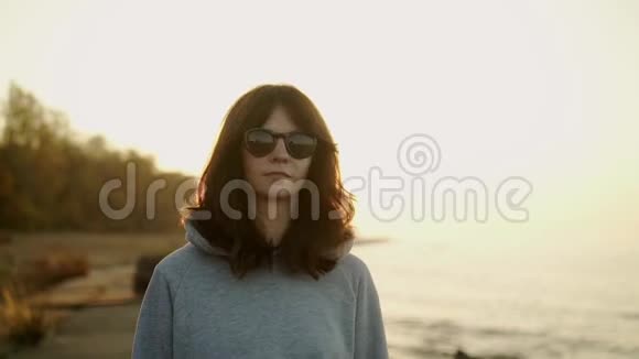 日落时分穿着灰色连帽衫的年轻女子在海滩上漫步视频的预览图