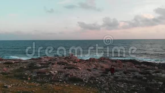 迷人的白种人女旅行者穿着红色衬衫穿过岩石海岸到日落的海边视频的预览图