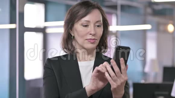 成功中年女商人用拳头在智能手机上庆祝的照片视频的预览图
