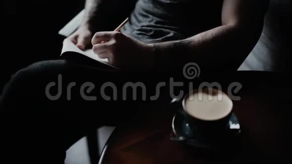 有纹身的男人在笔记本上写字喝杯咖啡和饮料视频的预览图