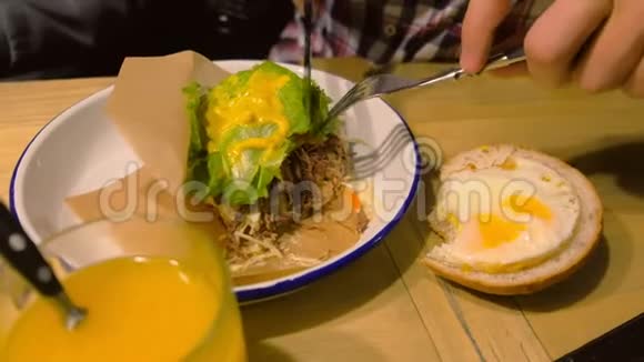 男人正在吃一个大汉堡盘子里有鸡蛋用叉子和刀子视频的预览图