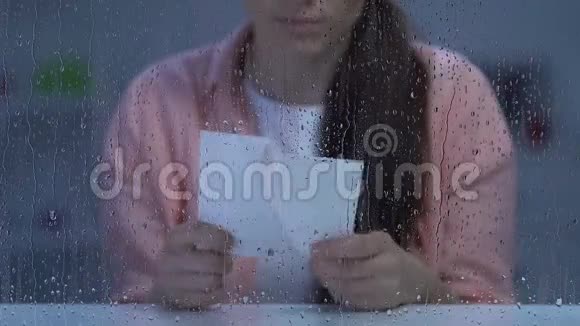 沮丧的女士拿着破照片靠近雨窗痛苦的离婚视频的预览图