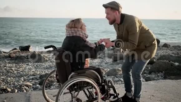 男人让坐在沙滩轮椅上的心爱的女人精神振奋视频的预览图